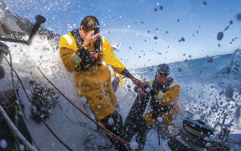 Sailors wearing Spinlock marine safety equipment on a boat approaching a big wave